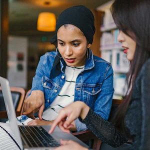 Two women collaborate on a laptop at a cafe, demonstrating the benefits of modern training resources.